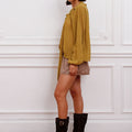 Blusa Klen Sofia Sarkany mostaza en modelo, estilo oversize, combinada con minifalda a cuadros y botas negras.