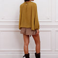 Blusa Klen mostaza Sofia Sarkany, mujer de espaldas luciendo blusa manga larga y pollera cuadrillé, look casual chic.