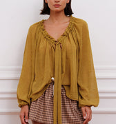 Blusa Klen mostaza Sofia Sarkany, escote V con volados, lazo y mangas largas. Look canchero y moderno.