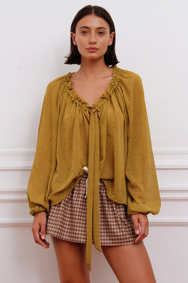 Blusa Klen mostaza Sofia Sarkany, escote V con volados, lazo y mangas largas. Look canchero y moderno.