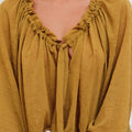 Blusa Klen Sofia Sarkany color mostaza, cuello en V con frunces y lazo. Textura original, look canchero.