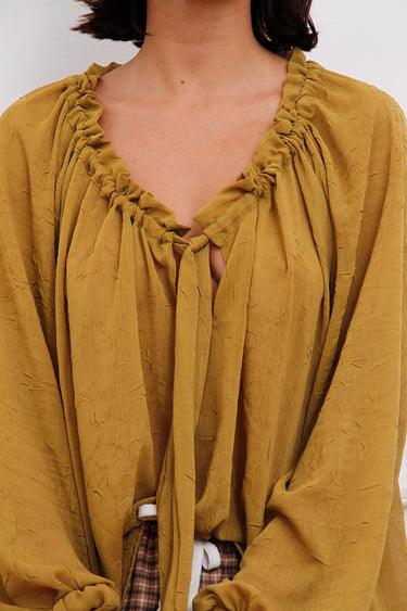 Blusa Klen Sofia Sarkany color mostaza, cuello en V con frunces y lazo. Textura original, look canchero.