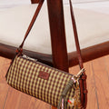 Cartera Loen Sofia Sarkany cuadriculada marrón y beige, con correa de cuero y llavero canchero, apoyada en una silla.