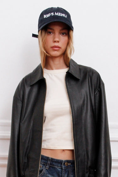 Gorra Kime Sofia Sarkany azul oscuro con letras blancas. Look urbano canchero con campera de cuero.