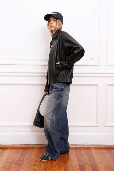 Modelo luciendo la Campera Rume negra de Sofia Sarkany, combinada con jeans anchos, gorra y cartera. Un look canchero.