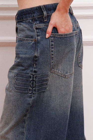 Detalle del Jean Strap Sofia Sarkany, denim azul con tiras decorativas laterales y mano en bolsillo. ¡Un toque distinto para vos!