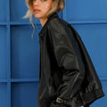 Modelo con campera Sofia Sarkany Traf negra de cuero sintético, combinada con jeans y fondo azul vibrante.